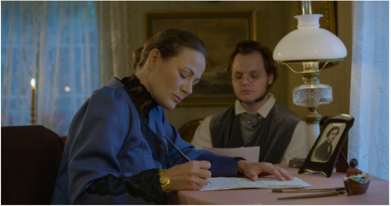 Kvinna sitter och skriver ett brev. Foto från filmen.