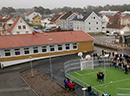 Skolbyggnad i gult tegel med en multiarena utanför.