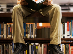 Person som sitter ovanpå en bokhylla och läser.